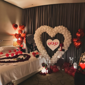 Romantic hotel room decoration with giant white heart balloon backdrop, candles and red heart balloons