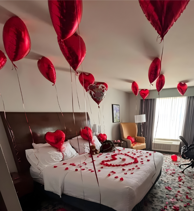 Romantic room decoration with red heart balloons, rose petals on bed, and heart shape bed design