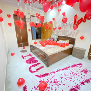 Romantic room decoration with red heart balloons, happy birthday foil letters and I Love You rose petal decoration