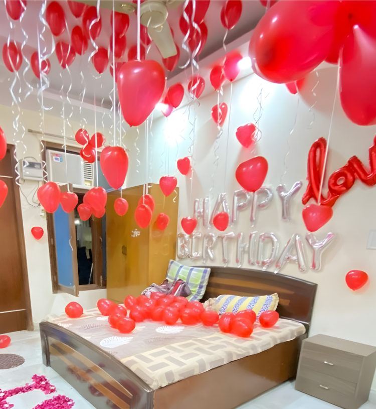 Romantic room decoration with red heart balloons, happy birthday foil letters and I Love You rose petal decoration